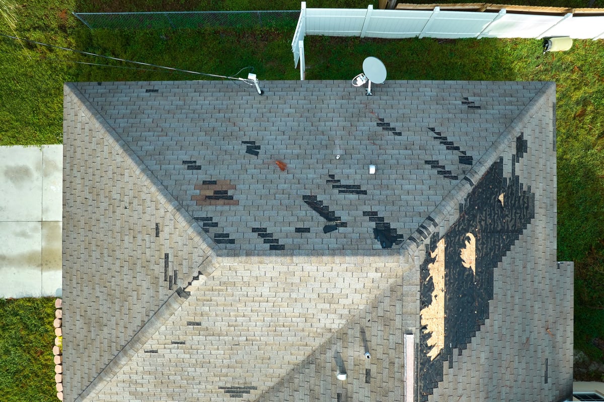 Worn residential roof with missing and damaged asphalt shingles before replacement