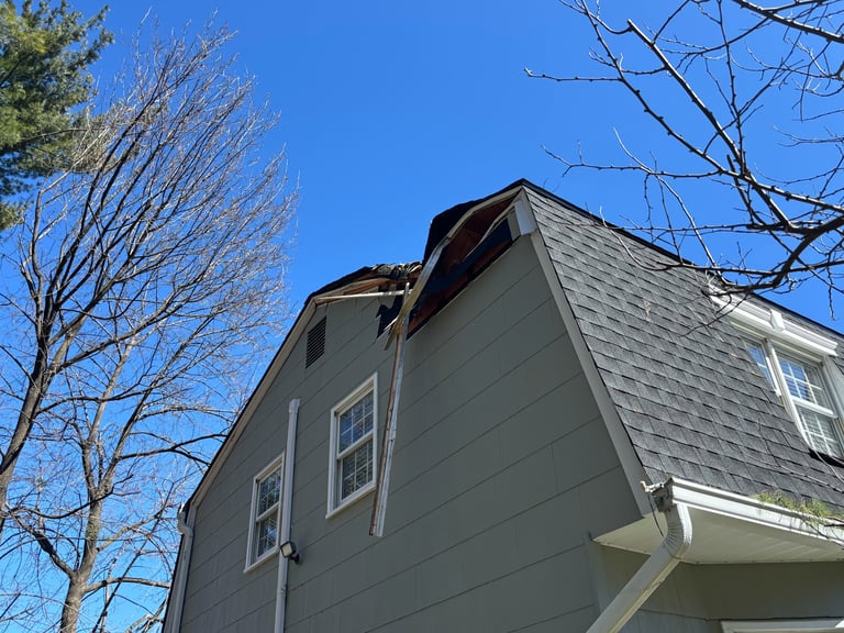 Two-story gray house with gable roof against clear blue sky, bare trees visible on sides