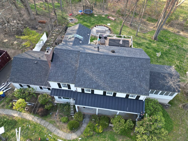 Aerial view of a modern residential home with gray roof surrounded by trees