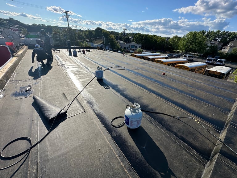 Workers applying waterproof membrane coating to a flat commercial roof