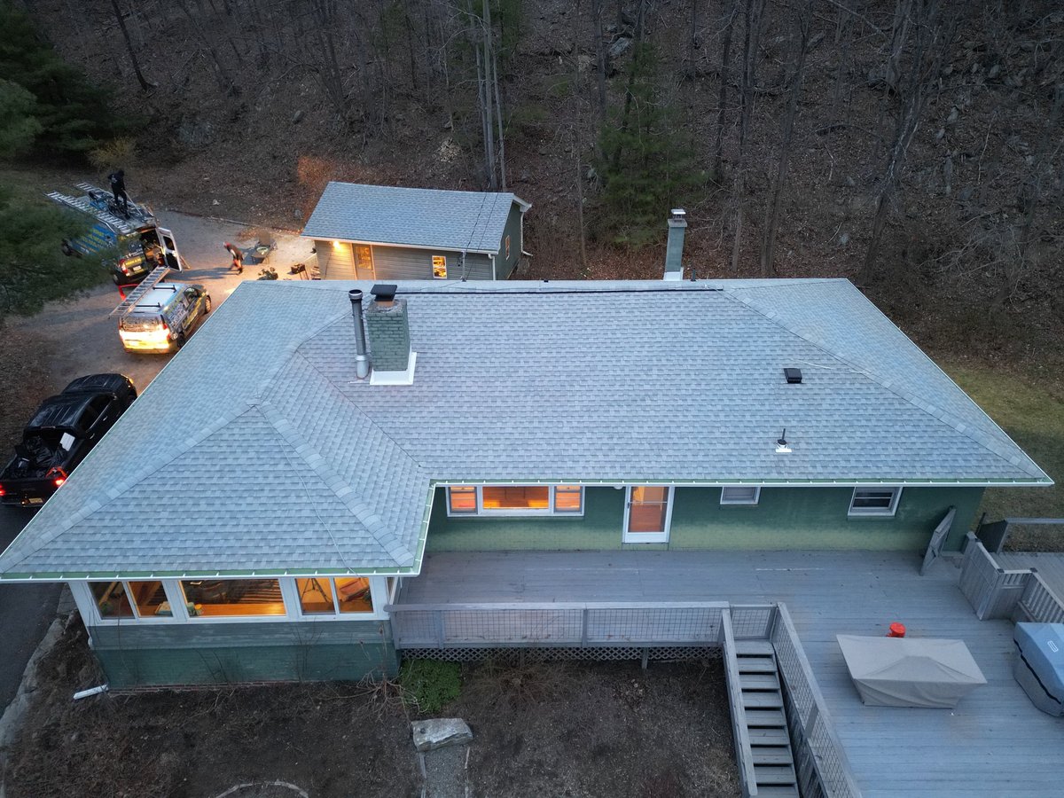 Aerial view of a modern house with gray roof and green exterior surrounded by trees and parked vehicles