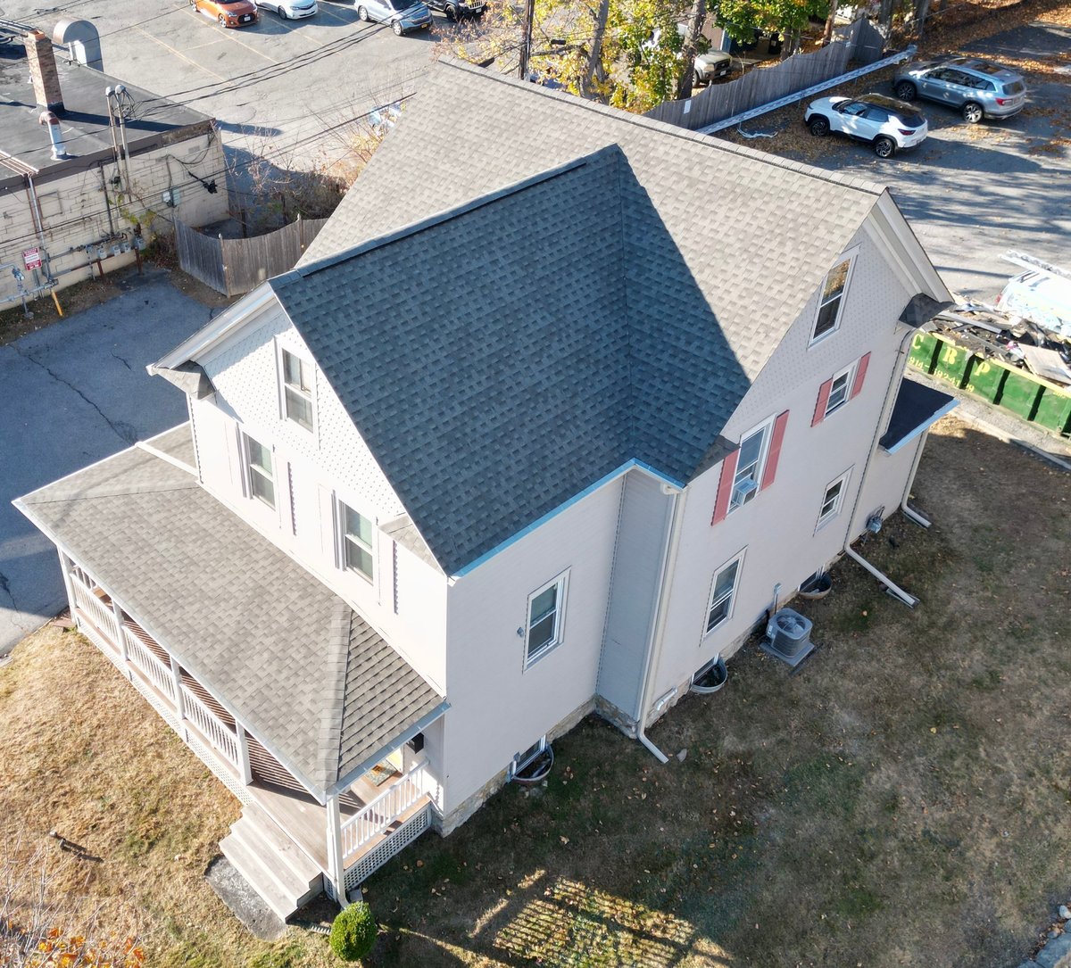 Aerial view of a white two-story house with dark blue roof and attached garage, situated in a residential neighborhood with parked cars and trees nearby