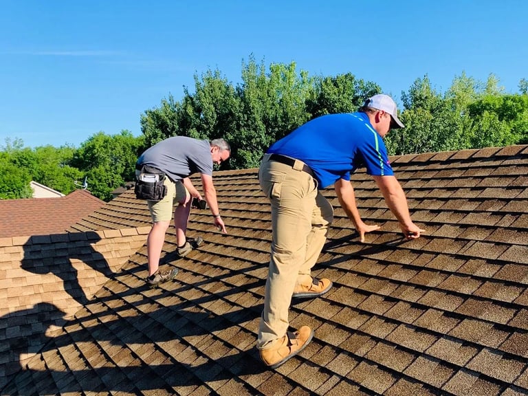 Two workers in safety gear inspecting a residential asphalt shingle roof